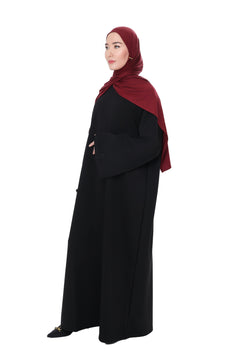 Model wearing the Comfy Dress in Black styled with a deep burgundy hijab, side view showcasing the relaxed oversized fit and wide sleeves.